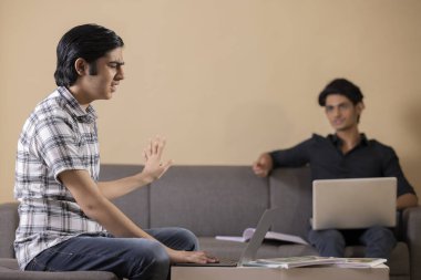 Evde dizüstü bilgisayar kullanarak ödev yapan iki mutlu genç çocuk.