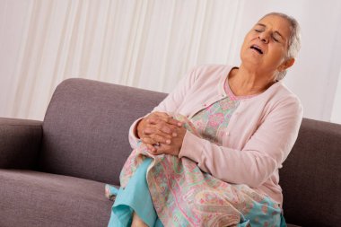 Kanepede otururken diz ağrısı çeken yaşlı bir kadın.