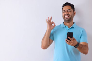 Neşeli genç adam akıllı telefon kullanırken el hareketi yapıyor.