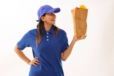 Portrait of delivery woman holding a bag of fresh vegetable against white background clipart