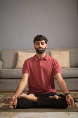 Genç adam oturma odasında meditasyon yapıyor.