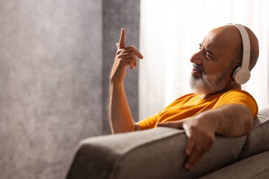 Oturma odasında kanepede otururken müzik dinleyip şarkı söyleyen son sınıf öğrencisi.