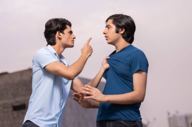 Genç bir çocuk diğerini gömleğinin yakasından tutup beyaz arka plana çekiyor.