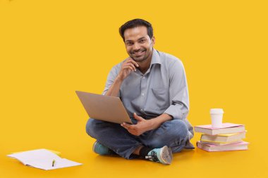 Dizüstü bilgisayarı kucağında otururken kameraya bakan mutlu genç adam.