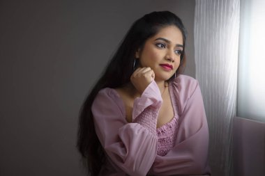 Pencerenin yanında oturan genç bir kadın ve elleri yanaklarında dışarı bakıyor.