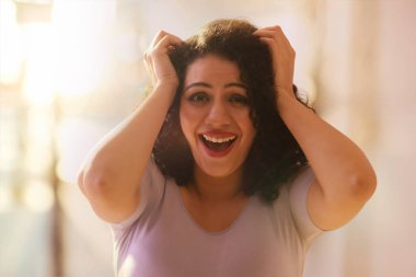 Yetişkin bir genç kadın iki eli başının üstünde gülüyor.