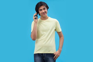 Mavi arka planda dikilirken Smartphone 'da konuşan mutlu bir gencin portresi