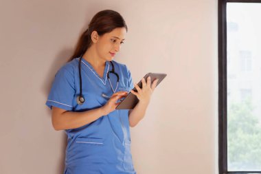 Hastanede dijital tablet kullanan mavi önlüklü kadın hemşire.