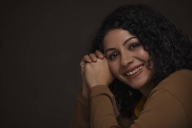 İki elinde de eğilmiş kameraya bakıp gülümseyen yetişkin bir kadın.