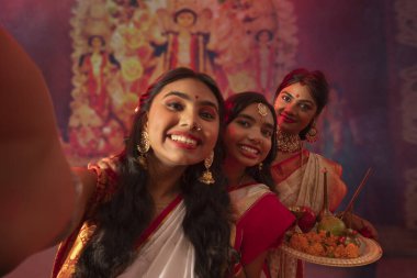 Bengalli kadın Durga Puja pandalında annesinin ve kız kardeşinin fotoğraflarını çekiyor.