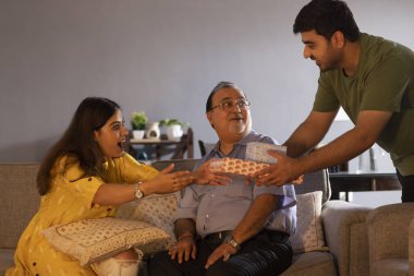 Abisi, babasıyla kanepede otururken kız kardeşine hediye veriyor.