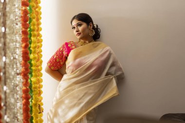 Beyaz sari giymiş Güney Hintli kadın duvarın önünde duruyor ve Onam için çiçek süslemesine bakıyor.