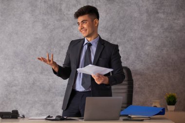 Portrait of young businessman with documents in hand standing in office clipart