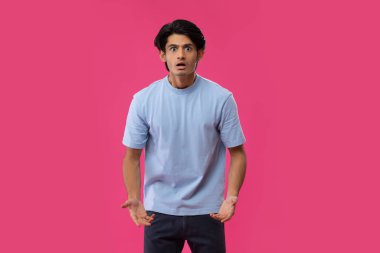 Pembe arka planda dikilirken el kol hareketi yapan şok olmuş bir gencin portresi.