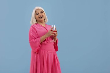 Bir bardak kırmızı şarapla ayakta duran neşeli yaşlı bir kadının portresi.