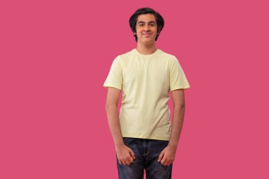 Pembe arka planda ayakta duran gülümseyen genç çocuğun portresi.