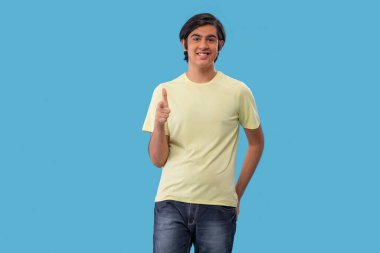 Mavi arka planda dikilirken kamerayı gösteren bir gencin portresi