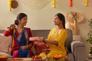 Durga Puja vesilesiyle oturma odasında kanepede otururken Bengali ailesi hediyelerini değiş tokuş ediyor.