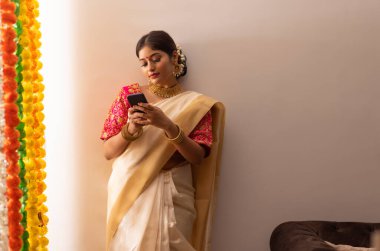 Beyaz elbiseli kadın duvarın önünde duruyor ve Onam 'da cep telefonu kullanıyor.