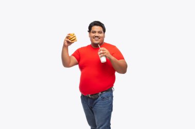 Portrait of a fat man holding a drink and burger in hand against plain background. clipart