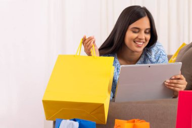 Kanepeye uzanmış elinde alışveriş torbasıyla tablet izleyen Hintli kız.