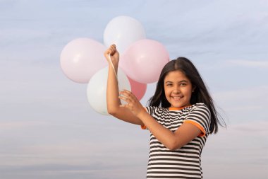 Neşeli kız mavi gökyüzüne renkli balonlar tutuyor