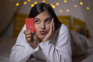 Indian girl posing with debit card while lying on bed clipart