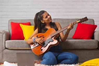 Genç kadın evde oturma odasında gitar çalmak