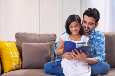 Bir baba ve kızı birlikte oturuyor ve kitap okuyorlar.