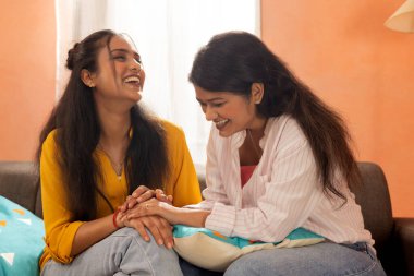 İki genç kadın oturma odasında kanepede otururken bir ışık anı paylaşıyorlar.