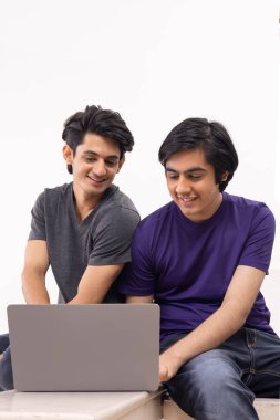 Düz arkaplanda dizüstü bilgisayar kullanan iki gencin portresi
