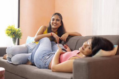 Oturma odasındaki kanepede dinlenen iki genç kadın.