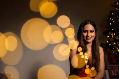 Gülümseyen kadın Noel ağacının yanında oturuyor.