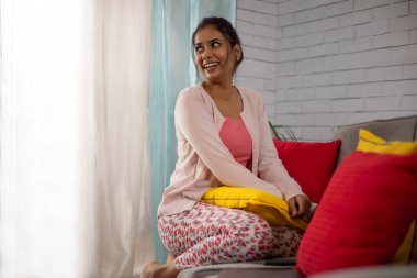 Oturma odasında kanepede otururken pencereden dışarı bakan neşeli kadın.