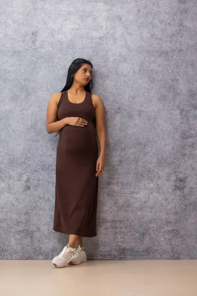 stock image Pregnant woman standing against wall with holding her stomach