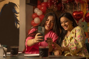 Kadınlar restoranda yan yana otururken cep telefonu kullanıyorlar.