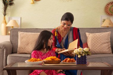 Anne ve kızı oturma odasında birlikte otururken kitap okuyorlar.