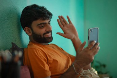 Genç adam, yatakta dinlenirken akıllı telefondan video görüşmesi yapıyor.