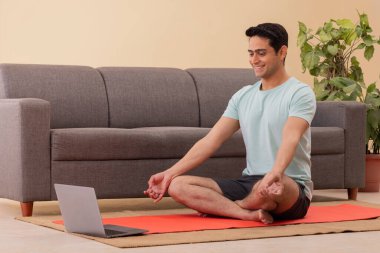 Erkek Hintli Yoga eğitmeni dizüstü bilgisayarla online bir ders veriyor.
