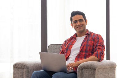 Kanepede dizüstü bilgisayarlı genç bir adamın portresi.