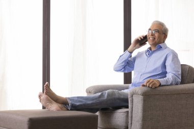 Evde kanepede dinlenirken cep telefonuyla konuşan mutlu kıdemli adam.