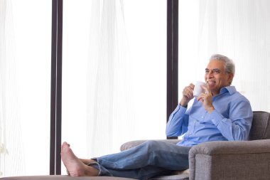 Evdeki kanepede dinlenirken kahve içen mutlu kıdemli adam.