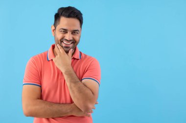 Mutlu bir gencin portresi, çenesinden tutarak mavi arka planda kameraya bakıyor.