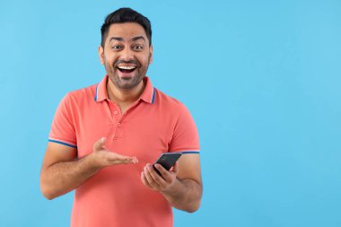 Kameraya bakıp akıllı telefonunu işaret eden mutlu bir gencin portresi.