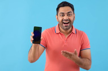 Akıllı telefonunu kameranın önünde gösteren neşeli bir gencin portresi.