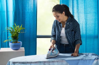 Odasında kıyafetlerini ütüleyen bir kadın..