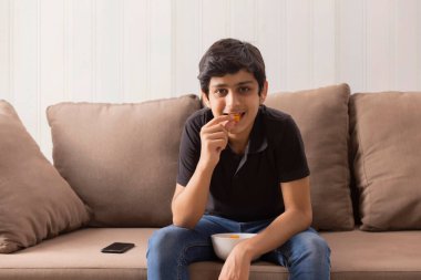 Akıllı bir ergen, evde oturup atıştırıyor ve yemek yiyor.