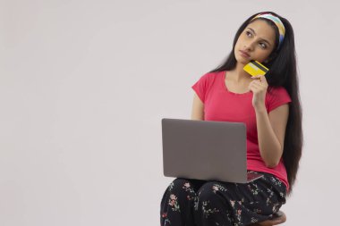 A TEENAGER SITTING AND THINKING WHILE DOING ONLINE SHOPPING clipart