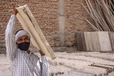 A MANUAL LABOURER WEARING FACE MASK LIFTING LARGE BLOCK OF TILE clipart