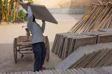 A DAILY WAGE LABOURER CARYING LARGE BLOCK OF TILE ON SHOULDER clipart